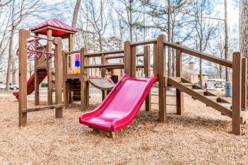 A playground with a red slide and wooden structure.